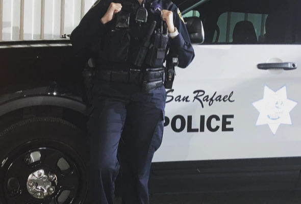 Officer Lorena Vega with the San Rafael Police Department smiles in uniform in front of her police vehicle
