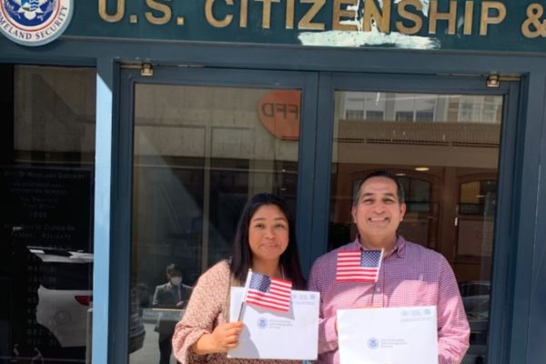 Two people with US flags and citizenship certificates in front of the US citizenship office
